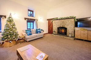 A cozy living room with a fireplace, a Christmas tree, a sofa, and a television.