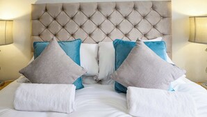 Una cama bien hecha con un cabecero capitonado, almohadas blancas y azules, y toallas blancas.