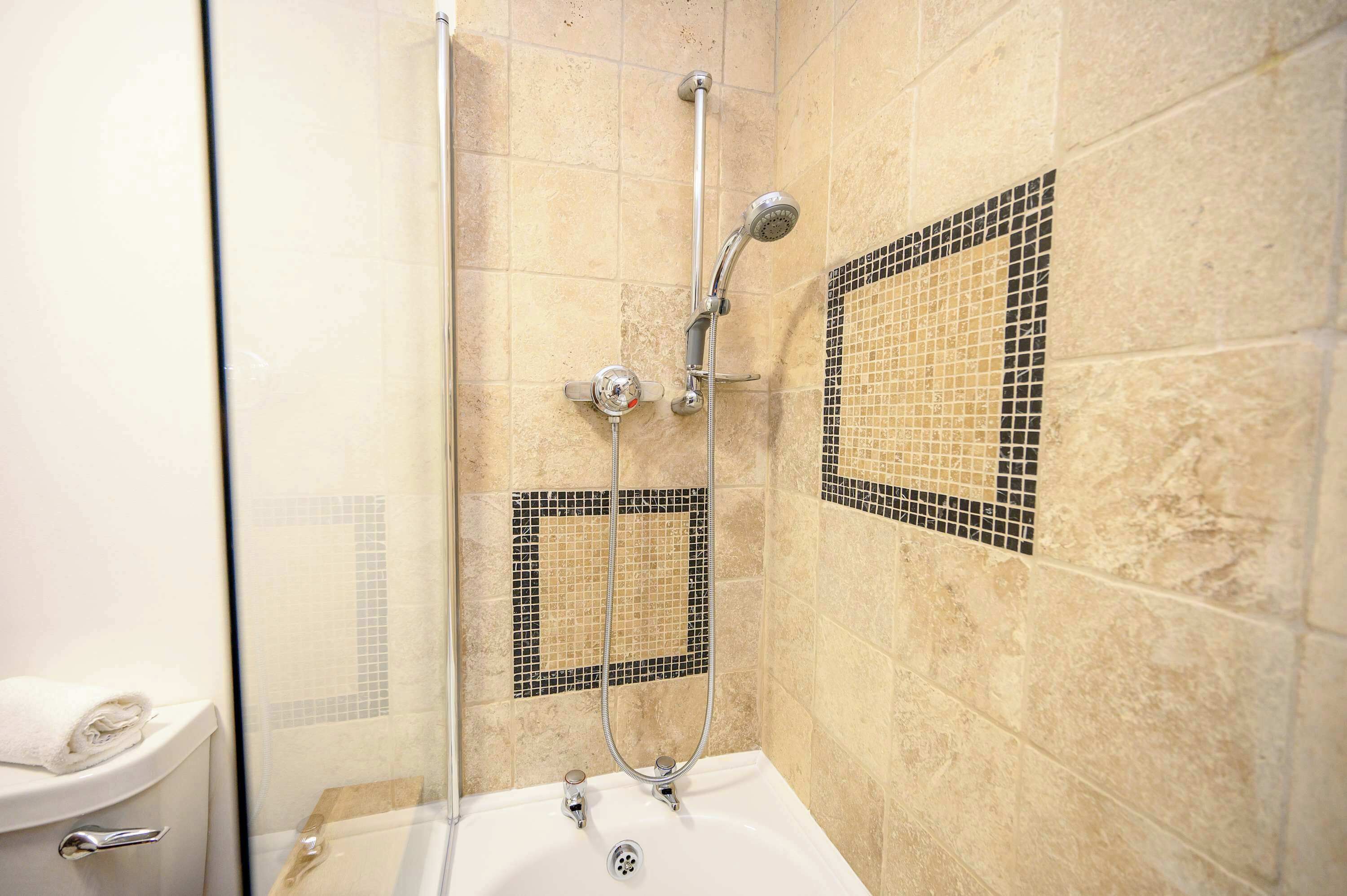 A shower with a glass door, a bathtub, and mosaic tile walls.