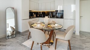 Een moderne eethoek met een glazen tafel, vier stoelen en een keuken op de achtergrond.