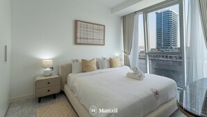 Een moderne hotelkamer met een groot bed, een nachtkastje met een lamp, een kunstwerk in een lijst aan de muur en uitzicht op een gebouw aan de overkant van het water.