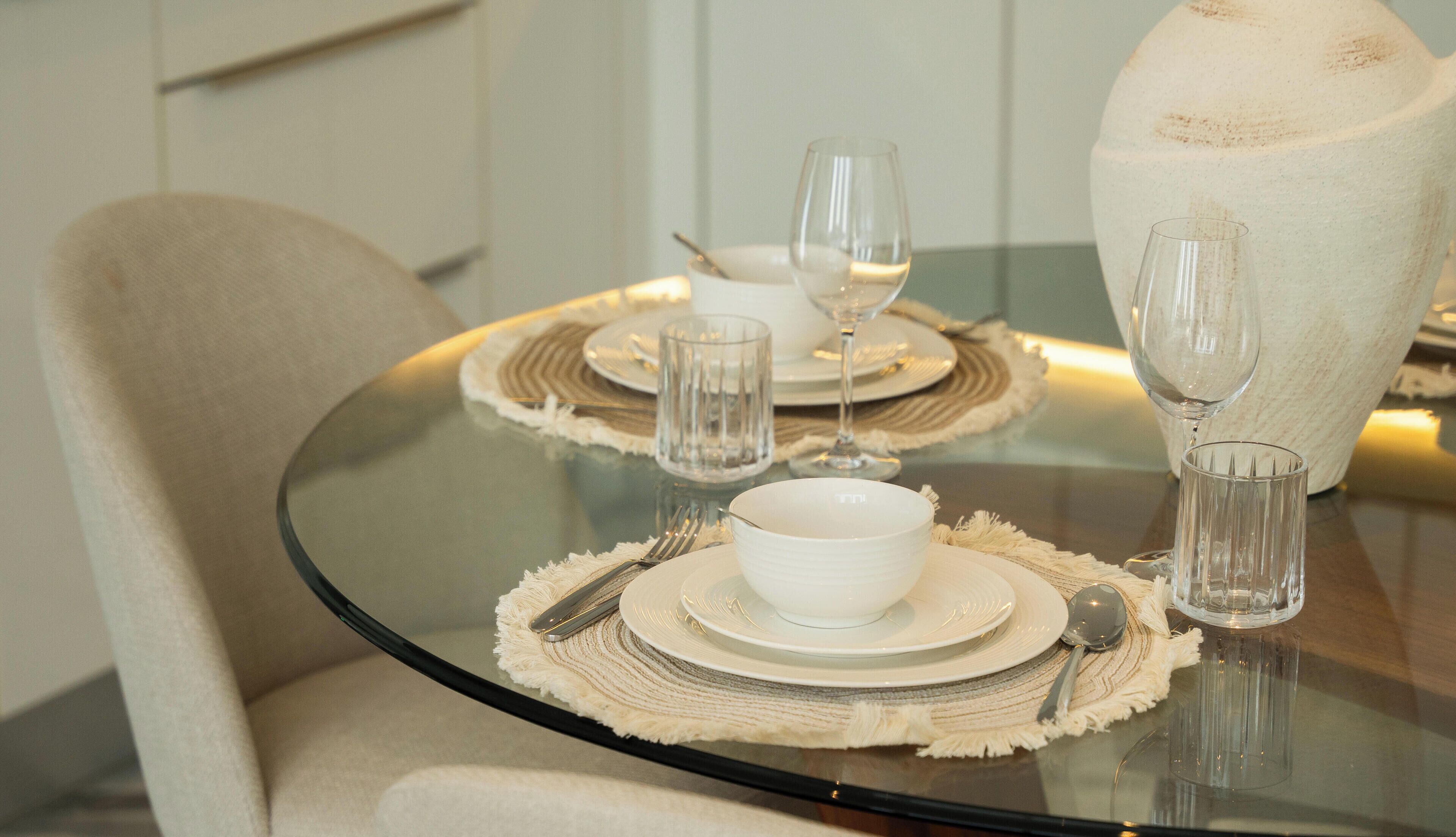Een eettafel gedekt met witte borden, kommen en bestek, inclusief wijnglazen en een vaas.