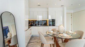 Een moderne keuken met witte kasten, een glazen eettafel en een grote spiegel.