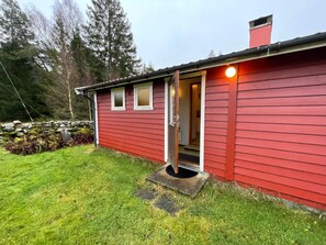 A red wooden house with a door open, a stone wall, and a grassy yard. - 4 Person Holiday Home in Kode (Kode)