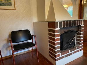 Quarto com lareira de tijolos, uma cadeira de madeira e um quadro na parede.