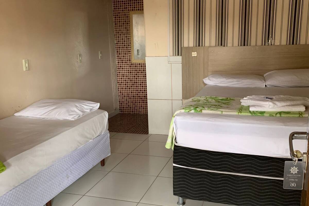 A hotel room with two single beds, a large window with blinds, a tiled floor, and a wooden headboard.