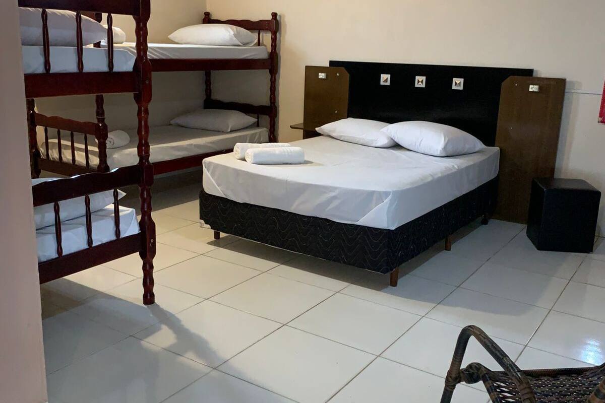 A room with a bunk bed, a single bed, a chair, and a speaker.