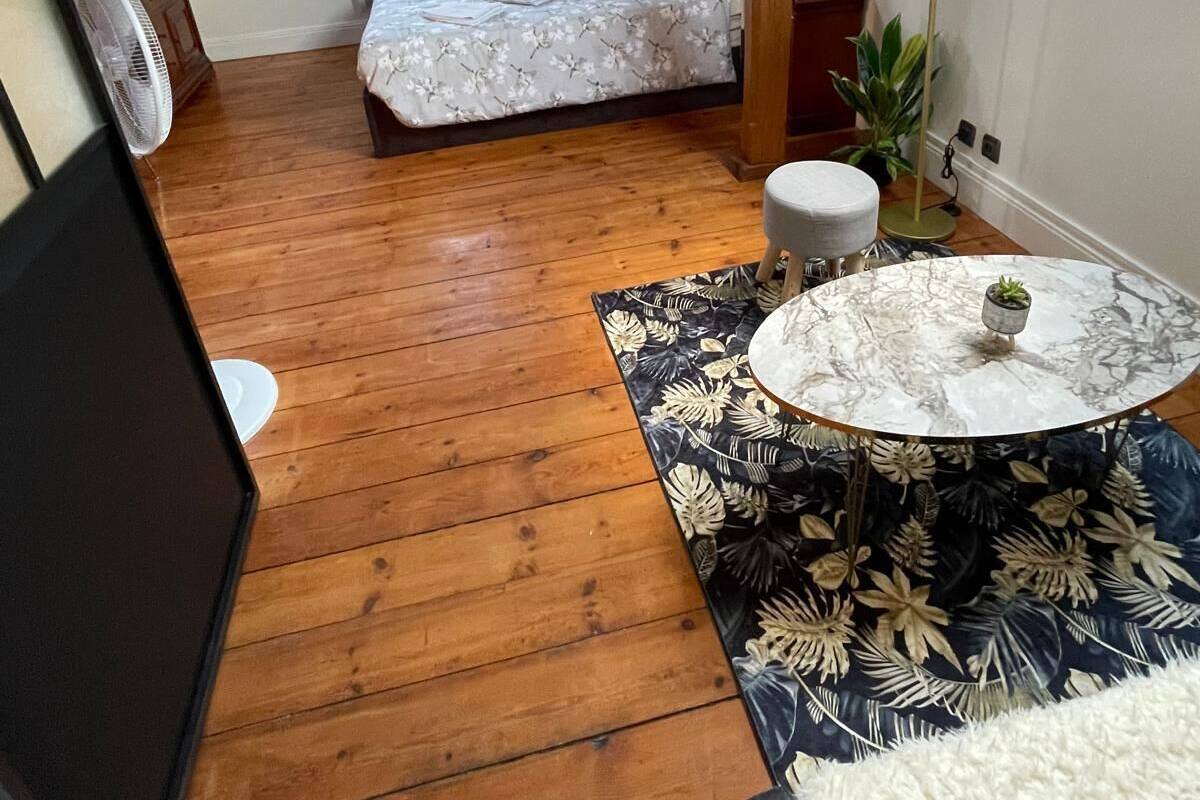 A compact bedroom with a skylight, a bed, a bedside table, a small round table with a plant, and a fan.