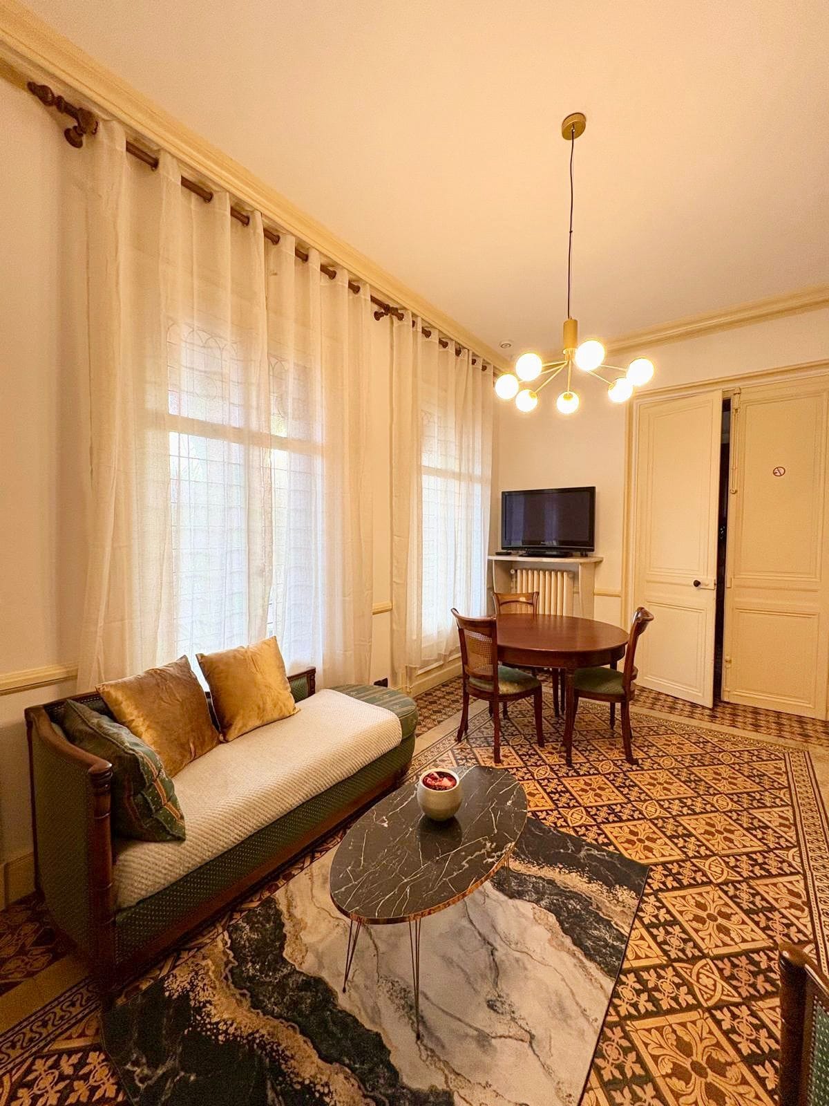 Ein Wohnzimmer mit einer Couch, einem Esstisch, Stühlen, einem Fernseher und einem gemusterten Boden.