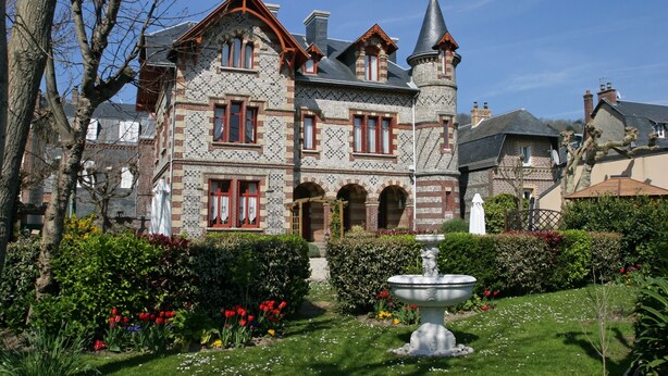 A large, historic building with a tower, surrounded by a well-maintained garden and a fountain. - La Villa Bligny (Étretat)