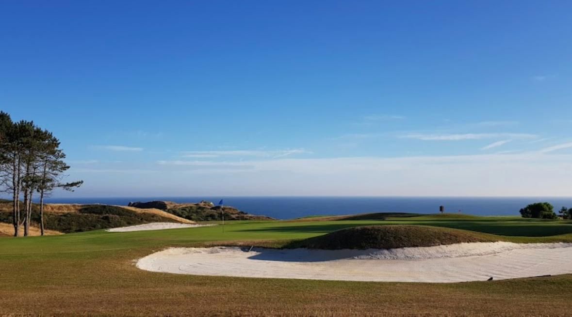 A golf course with sand bunkers and a clear view of the ocean.