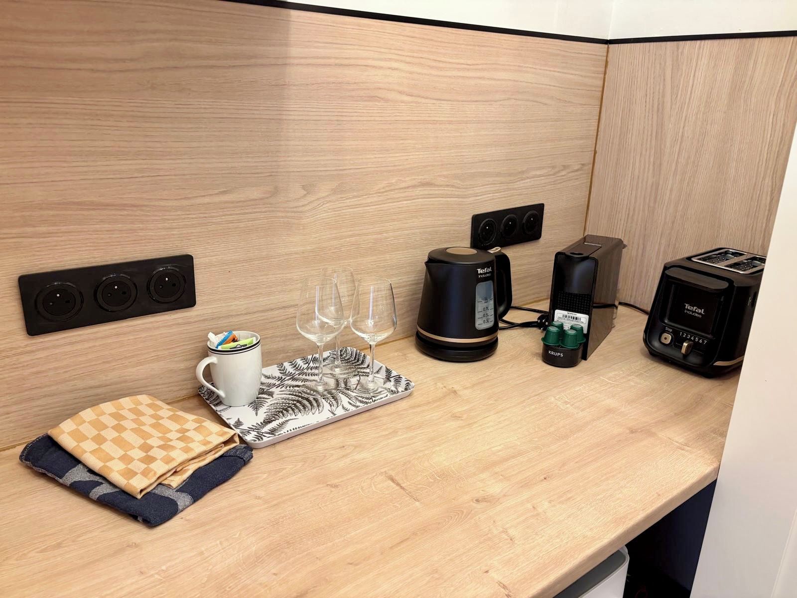 Ett litet kök med en kaffebryggare, brödrost och vattenkokare på en bänkskiva i trä.
