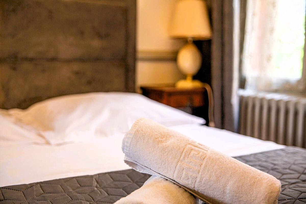A neatly made bed with a white pillow and a rolled towel on the side.