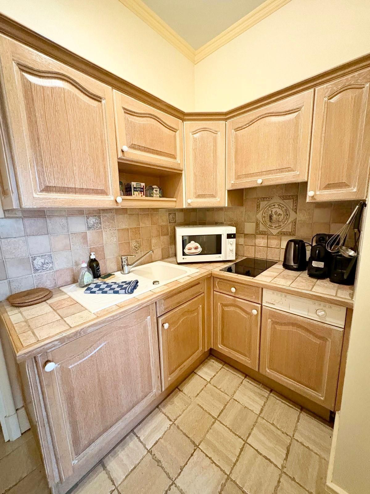 A compact kitchen with wooden cabinets, a microwave, a coffee maker, and a sink.