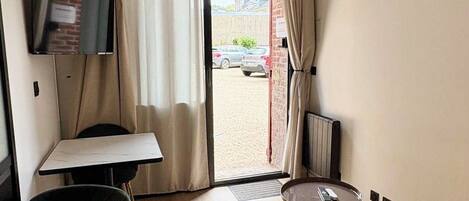 A hotel room with a bed, a small table, a chair, a ceiling fan, a TV, and a view of the outside.