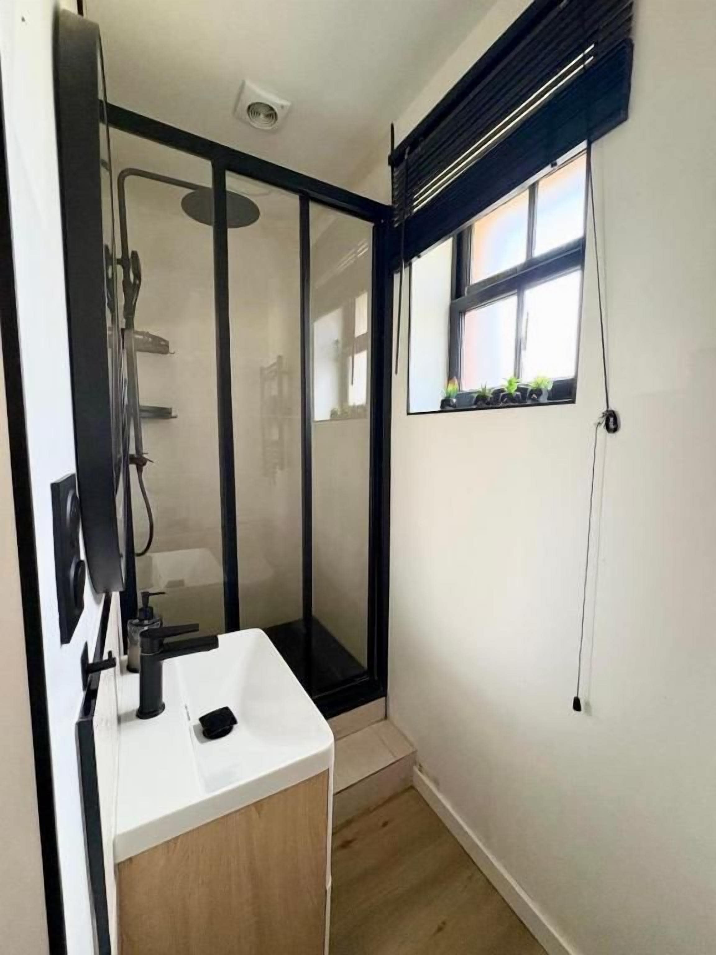 A bathroom with a shower, a sink, and a window.