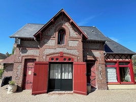 A traditional brick building with a red door and window frames, a gabled roof, and a small porch area.