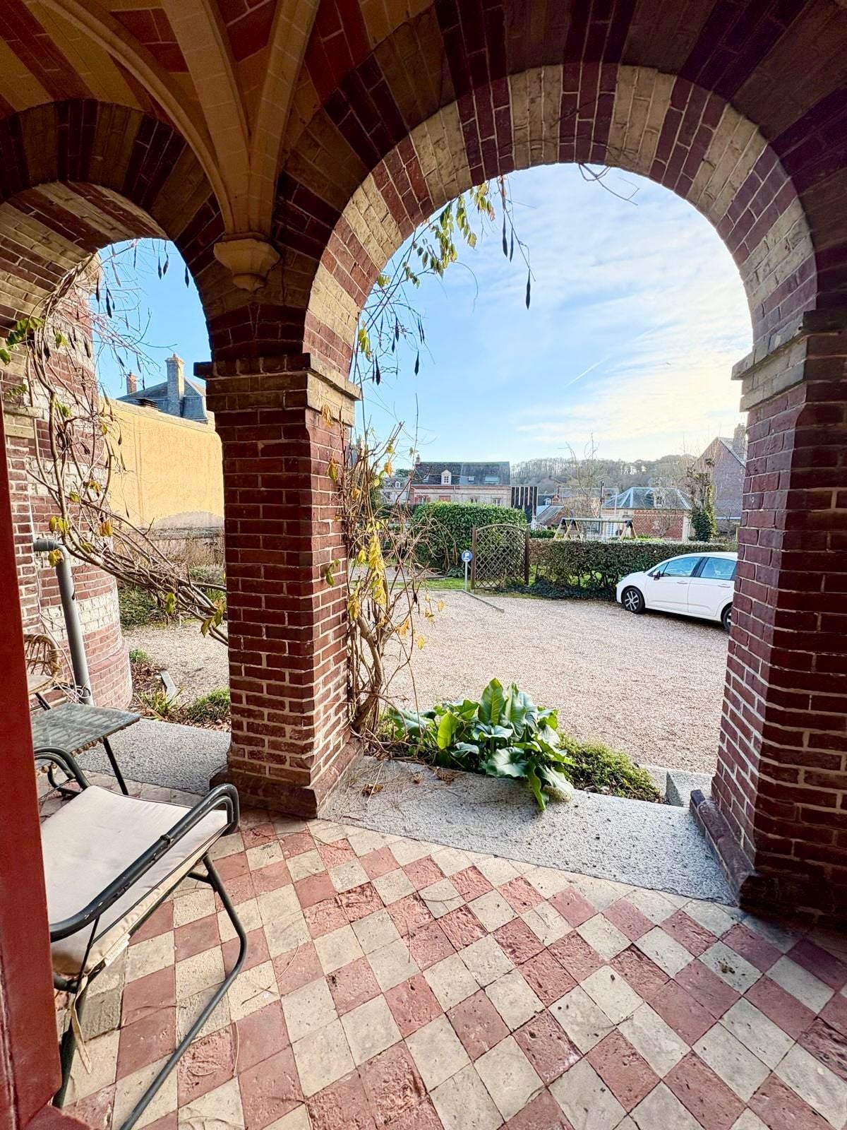 An outdoor patio area with brick arches, a metal table, and a car parked in the background.
