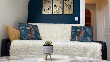 A living room with a dark blue accent wall, a white fluffy sofa, two tiger-themed pillows, a small potted plant, and a marble coffee table.