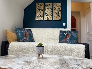 A living room with a dark blue accent wall, a white fluffy sofa, two tiger-themed pillows, a small potted plant, and a marble coffee table. - La Villa Bligny (Étretat)