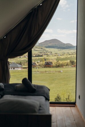 Une chambre avec une grande fenêtre, un lit et une vue sur un paysage rural avec des maisons et une colline.