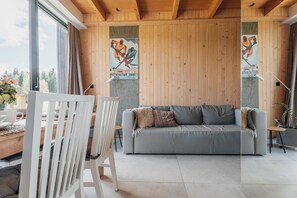 Un intérieur moderne avec un plafond en bois, un canapé gris, des chaises blanches et une table sur laquelle est posé un vase de fleurs.