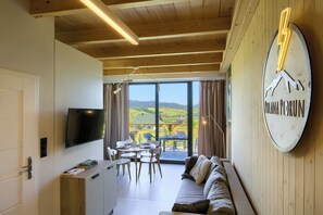 Une chambre moderne équipée d’une télévision, d’une table à manger et d’un canapé, avec de grandes fenêtres offrant une vue sur la campagne.