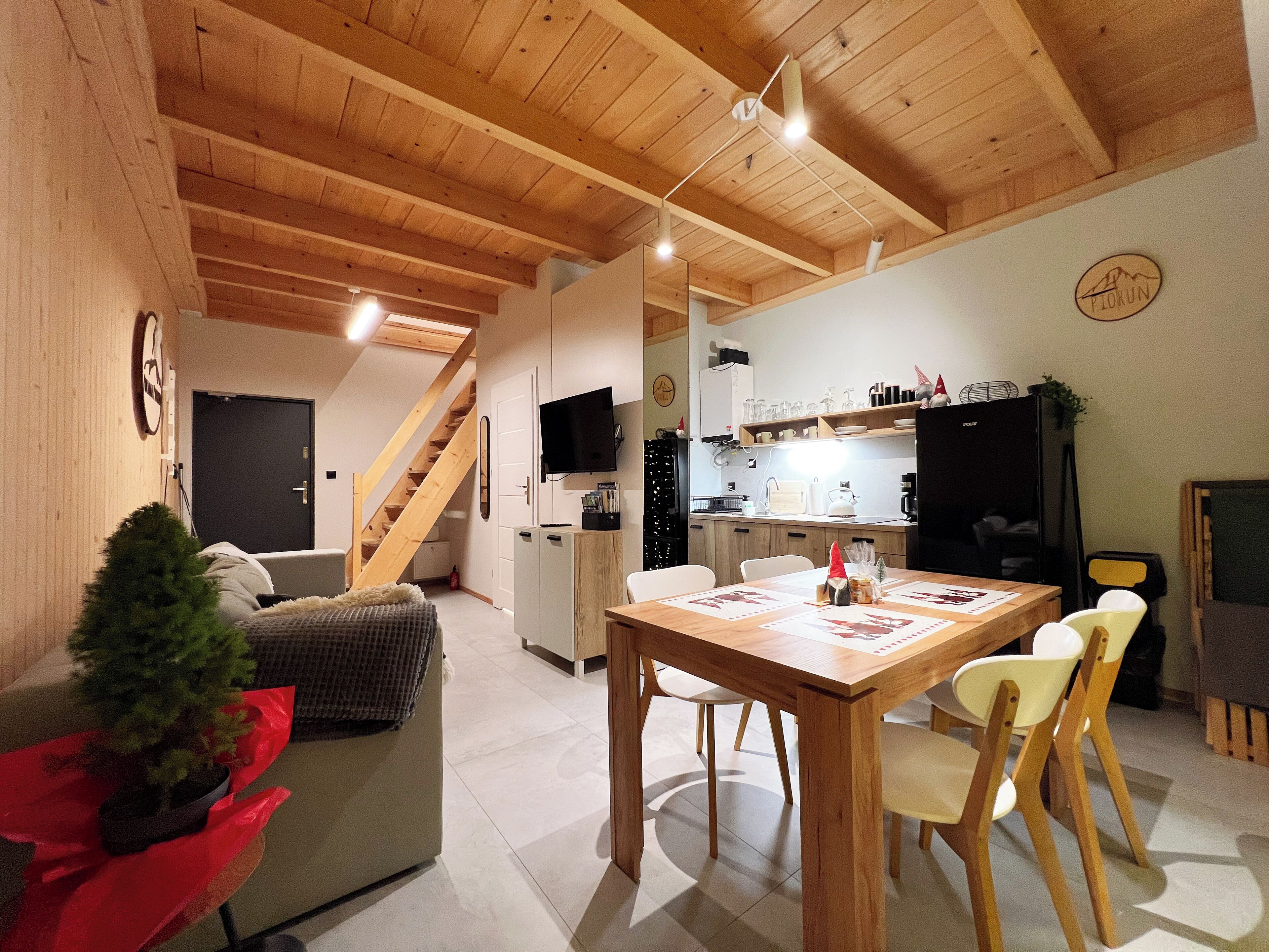 A cozy interior with a wooden ceiling, a dining area with a table and chairs, a kitchen with appliances, and a staircase leading to another level.