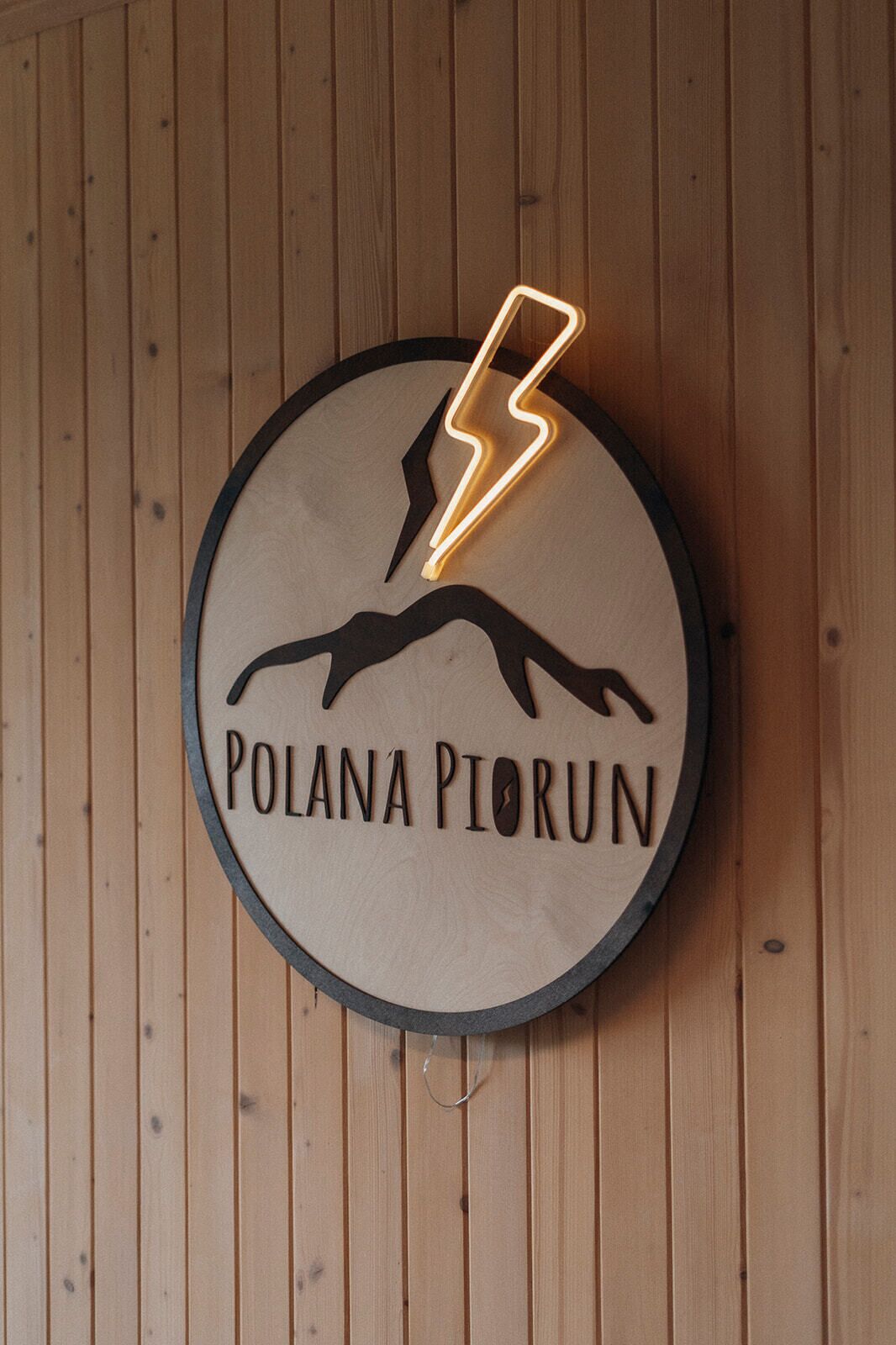 Una señal circular con un rayo y el texto 'POLANA PIORUN' en una pared de madera.