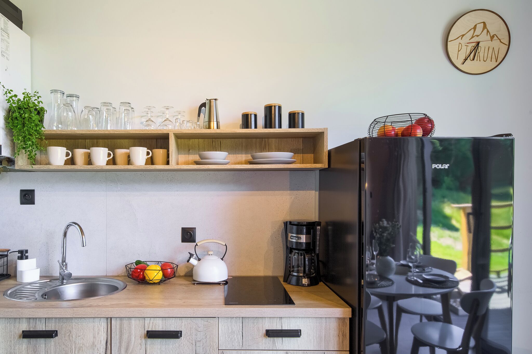 A modern kitchen with a sink, kettle, coffee maker, and a refrigerator.
