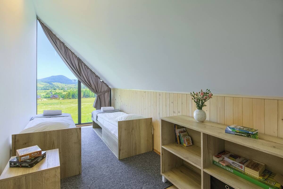 Un dormitorio con cama, un escritorio pequeño, una estantería y un ventanal que ofrece vistas a un paisaje verde.