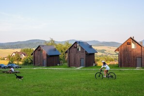 Entorno rural con graneros de madera, un campo cubierto de césped y un ciclista.