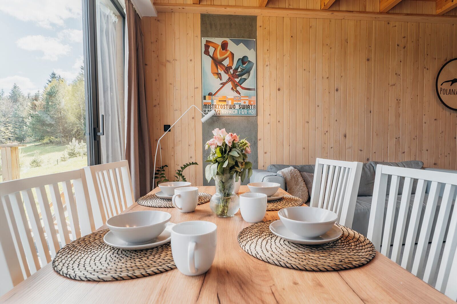 A wooden dining table with white chairs, bowls, and a vase of flowers.