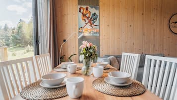 A wooden dining table with white chairs, bowls, and a vase of flowers.