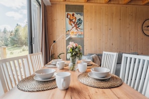 Une table à manger en bois, avec des chaises blanches, des bols et un vase rempli de fleurs.