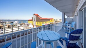 Un balcón con sillas azules y una mesa, con vista a un puerto deportivo con barcos y un edificio amarillo con un letrero que dice 'FISHING'.