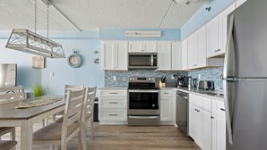 A modern kitchen with white cabinets, a stainless steel refrigerator, and a blue-tiled backsplash. - Two-bedroom oceanfront with indoor and outdoor pools! (Ocean City)