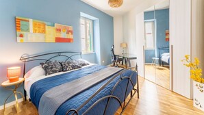 Quarto com cama, mesa de cabeceira, abajur e obra de arte na parede.