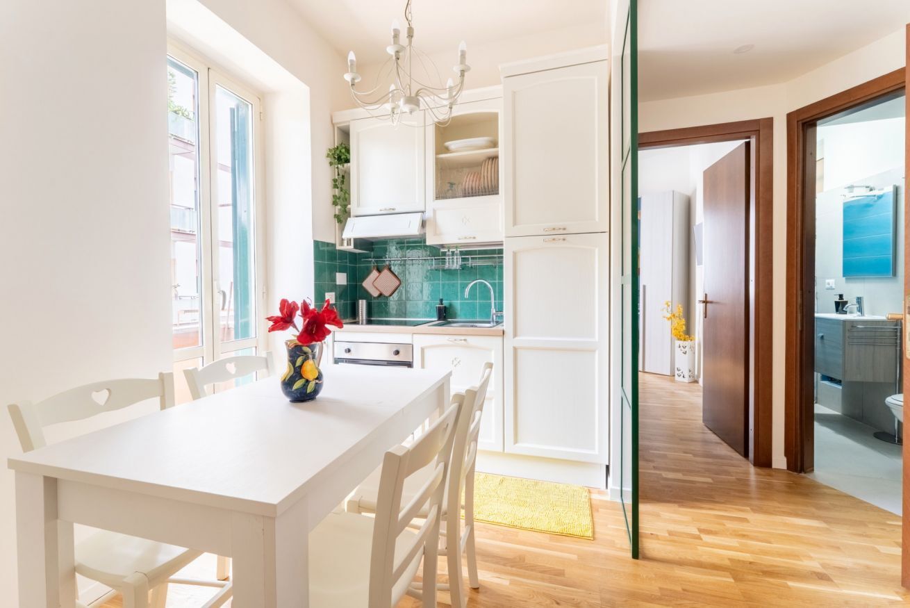 Une cuisine moderne avec des meubles blancs, une table à manger avec des chaises et un vase rempli de fleurs.