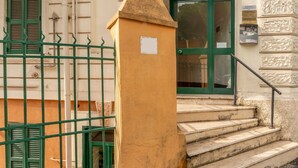 Entrada de um edifício com portão verde, escadaria de pedra e porta com persianas verdes.