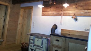 A rustic kitchen with wooden walls, a vintage stove, and hanging kitchen utensils. - Chalet Hühnerstall am Soderhof - peace and quiet and private SPA in the Salzburg mountains (Unken)