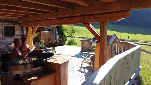 A wooden deck with a hot tub, outdoor seating, and a view of a green landscape. - Chalet Hühnerstall am Soderhof - peace and quiet and private SPA in the Salzburg mountains (Unken)