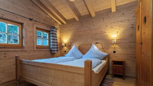 A wooden cabin bedroom with a bed, two wall-mounted lamps, a window with curtains, and a small nightstand. - Chalet Hühnerstall am Soderhof - peace and quiet and private SPA in the Salzburg mountains (Unken)