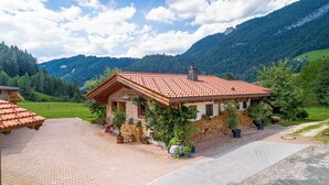 A traditional wooden house with a red-tiled roof, surrounded by lush greenery and mountains. - Chalet Hühnerstall am Soderhof - peace and quiet and private SPA in the Salzburg mountains (Unken)