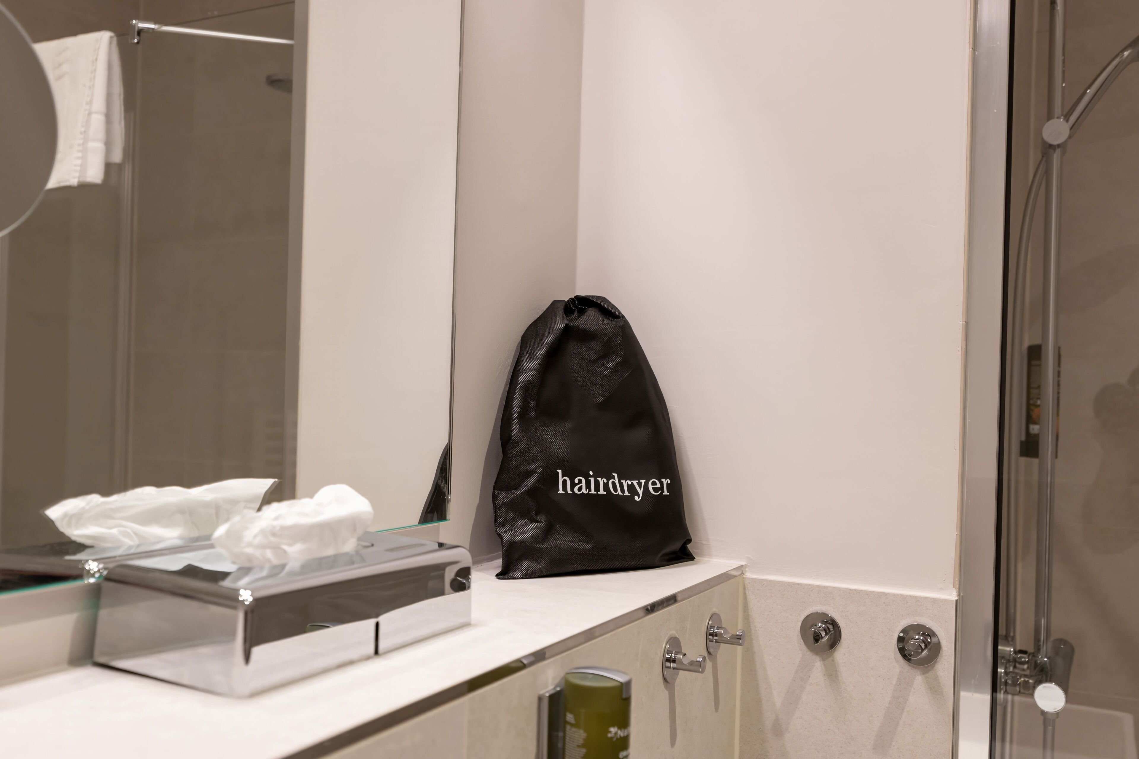 A bathroom with a towel rack, a mirror, a hairdryer bag, a tissue box, and a shower.