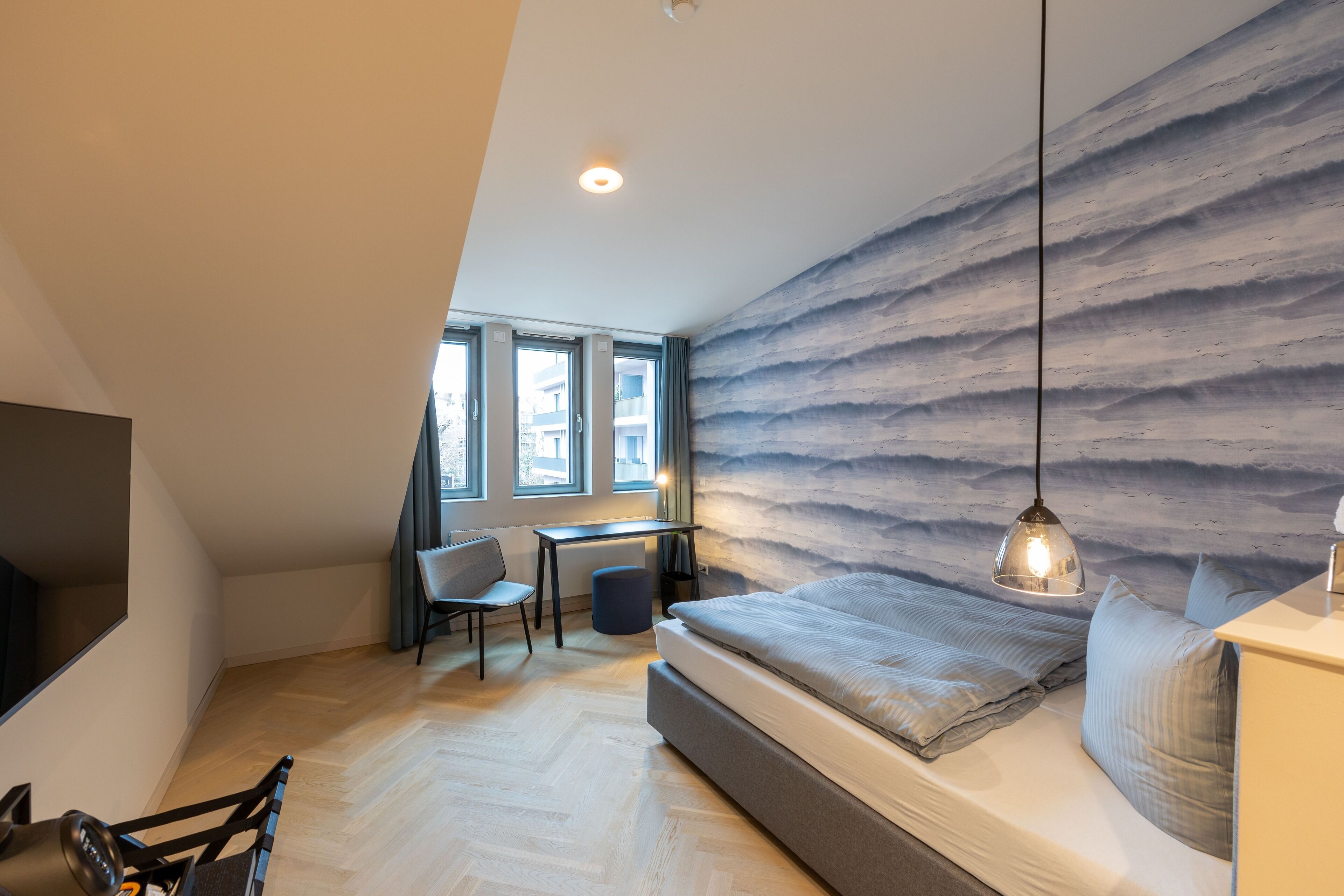 Un dormitorio con cama, escritorio, silla y vistas al exterior a través de amplios ventanales.