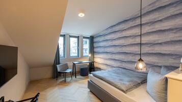 Un dormitorio con cama, escritorio, silla y vistas al exterior a través de amplios ventanales.
