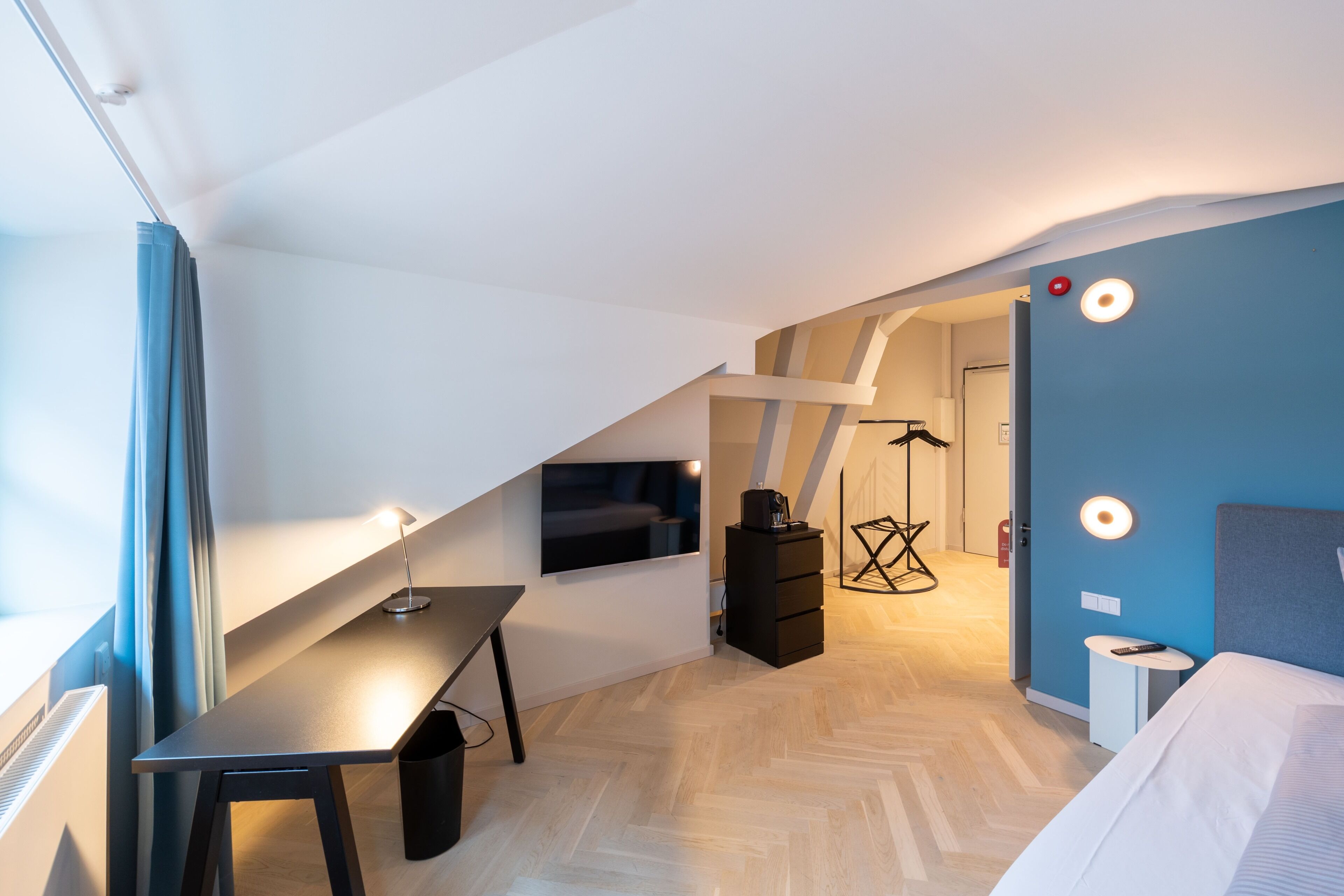 A modern room with a desk, bed, and a staircase leading to another level.