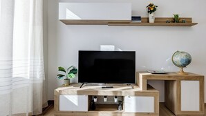 A modern living room with a flat-screen TV, wooden side tables, and shelves with decorative items. - Testaccio Patty Flat (Rome)
