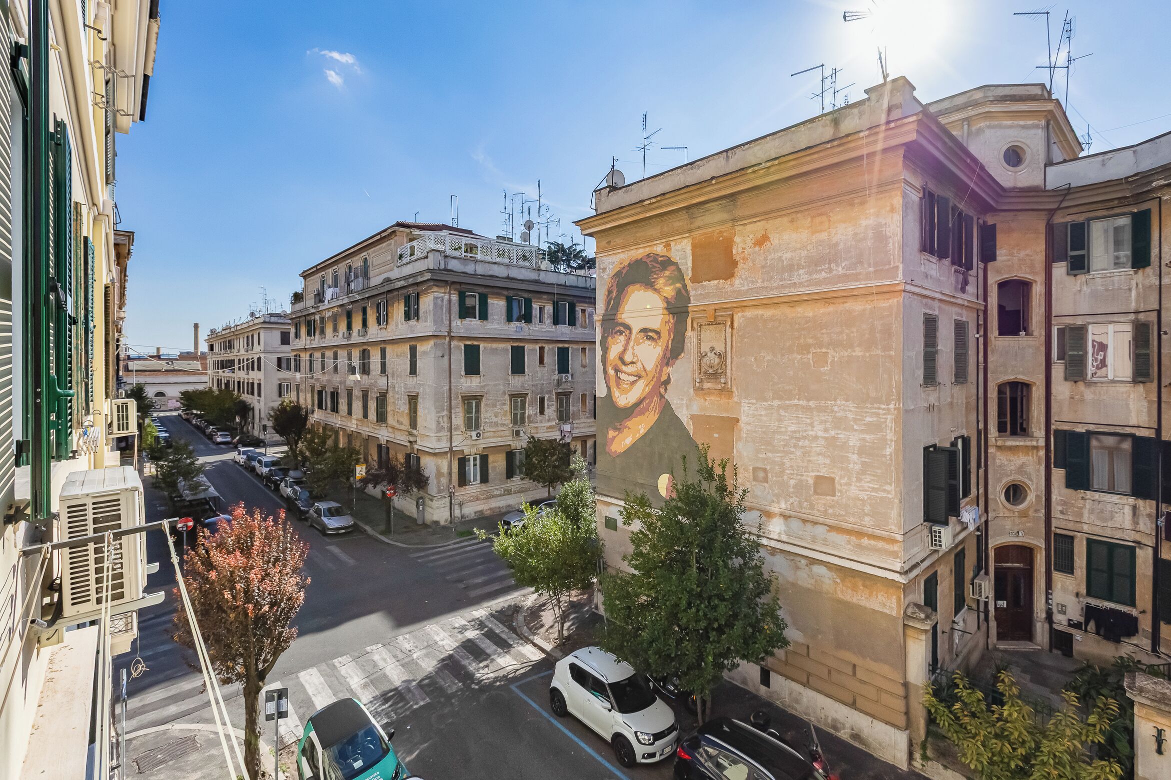 A street view with a building featuring a mural, parked cars, and a clear sky.